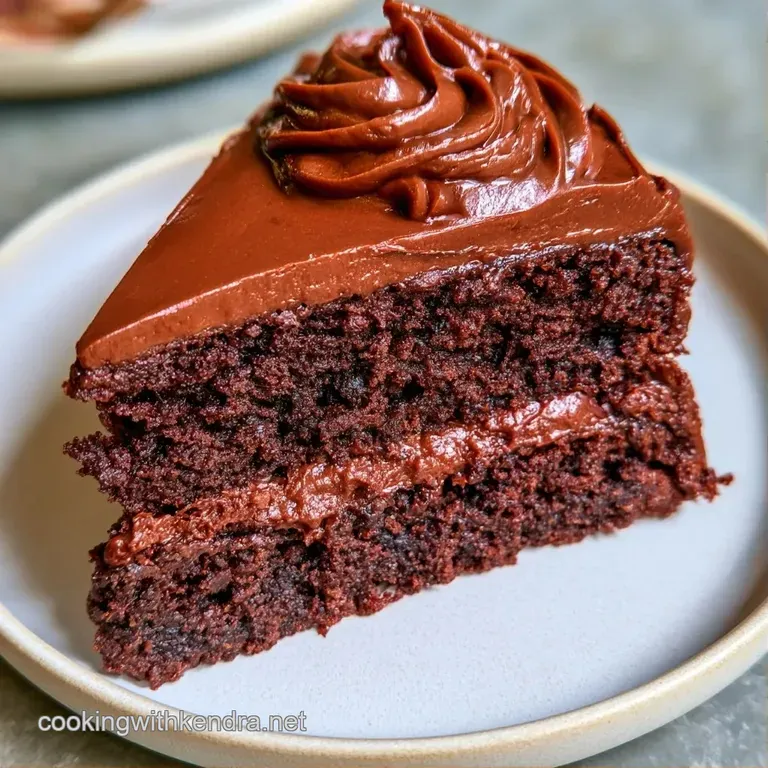 Elegant slice of dark cocoa cake on a white plate, garnished with tart raspberries and a drizzle of syrup.