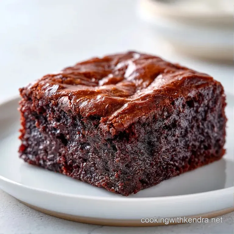 A slice of moist chocolate cake dusted with powdered sugar on a white ceramic plate with a fresh mint leaf.
